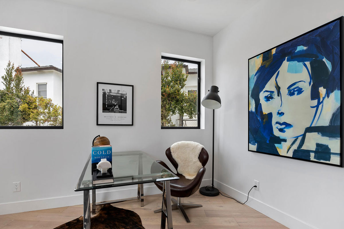 Corner of staged room with glass table, windows and framed artwork.