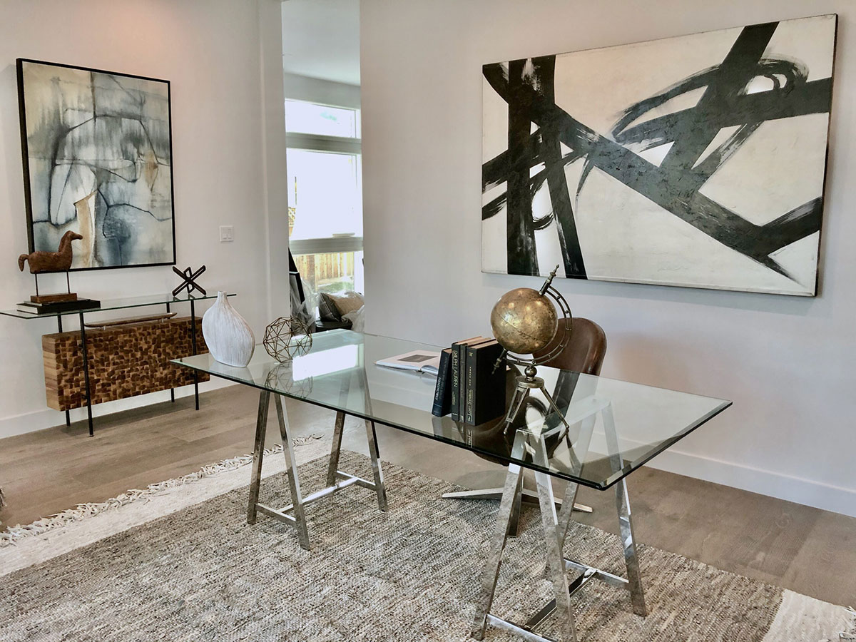 Staged home office with glass table and paintings.